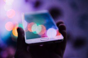 white iphone in hand with colorful bokeh bubbles floating around