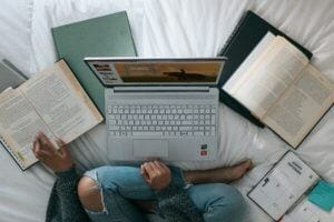 a woman sits over a laptop with books spread out around her