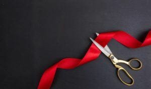 Top view of gold scissors cutting red silk ribbon against black background